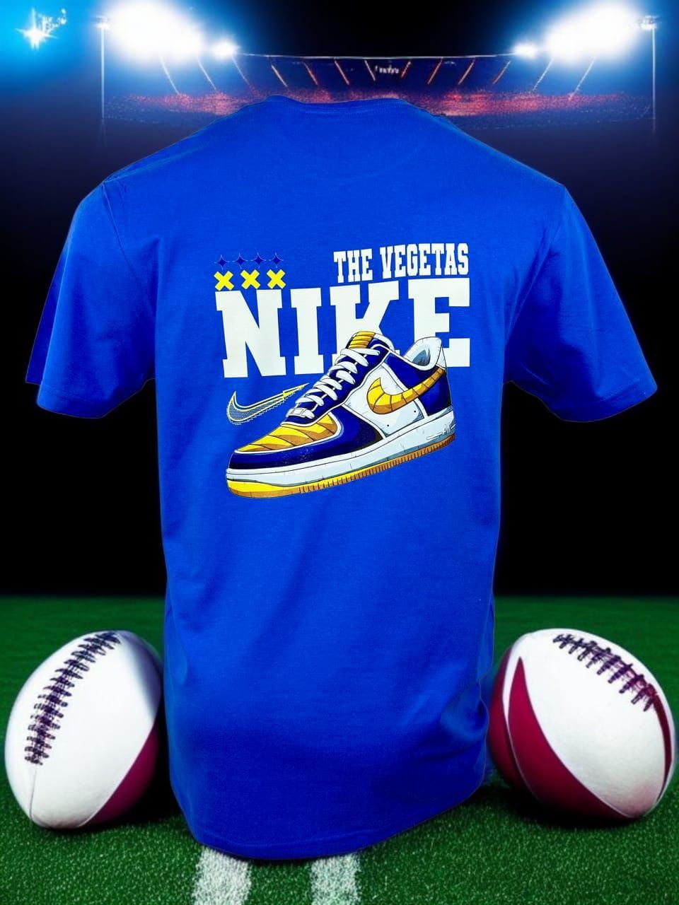 Camiseta azul de fútbol Nike con gráfico blanco, mostrada con dos balones de fútbol en un campo bajo las luces del estadio.