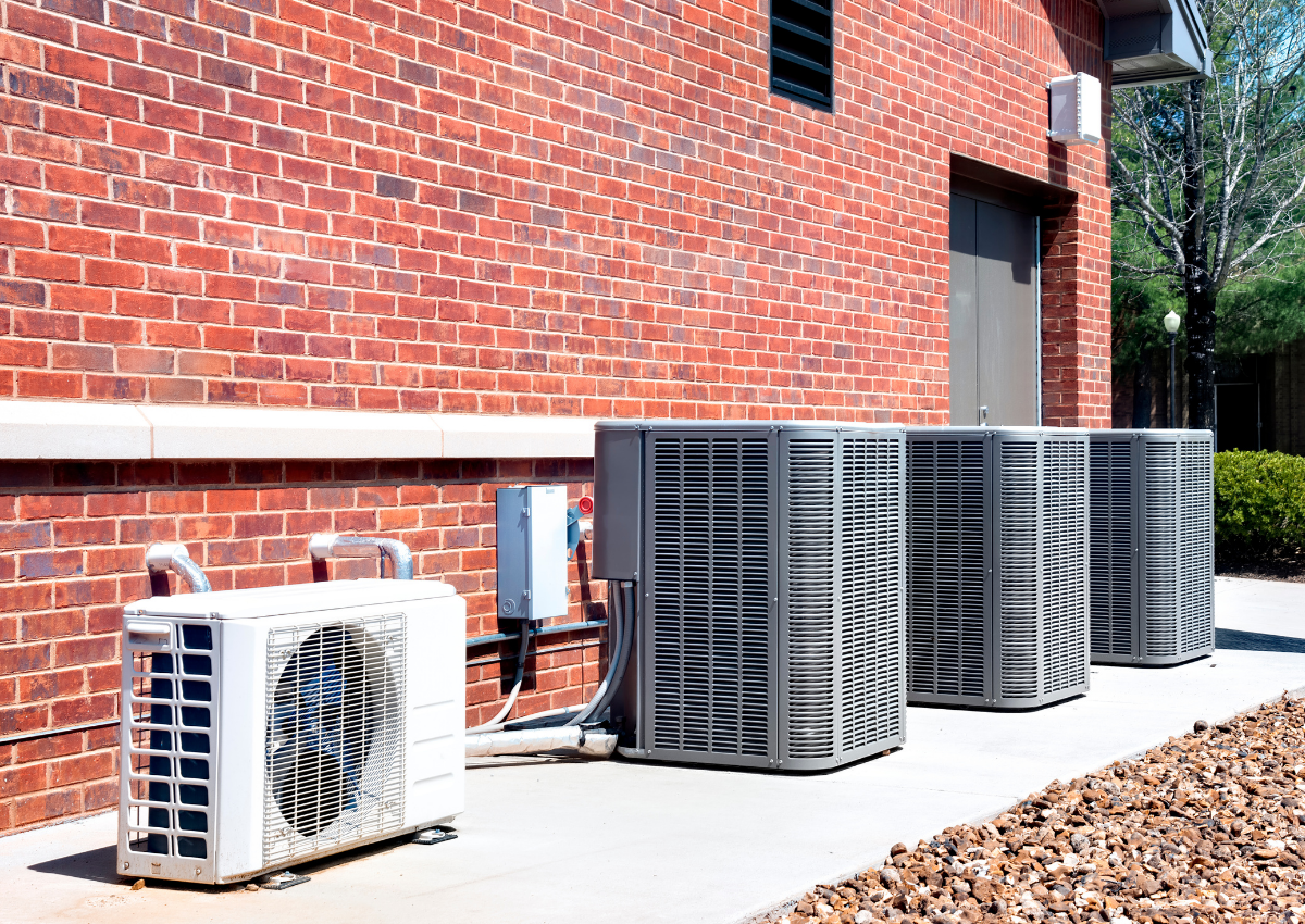 Outdoor air conditioning units beside a red brick building on a concrete pad