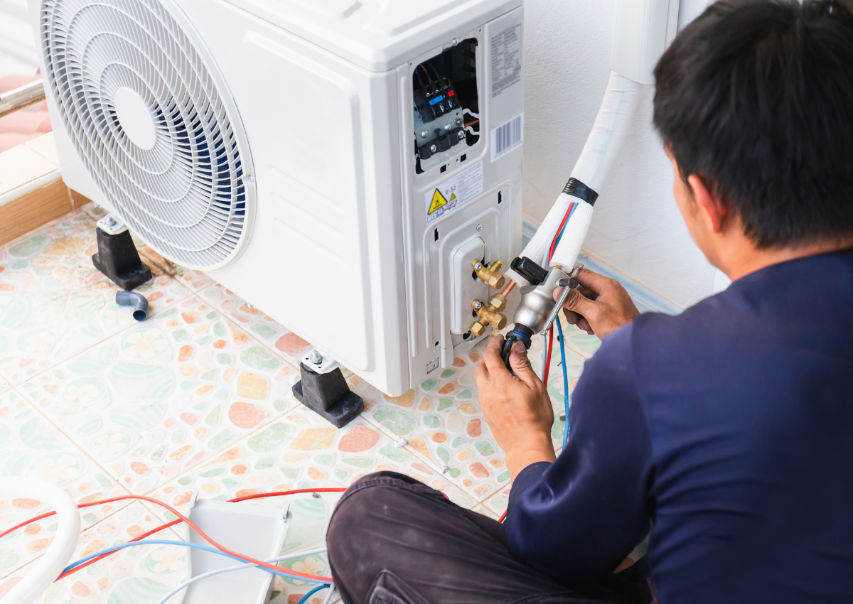 Technician repairing an outdoor air conditioner unit with tools beside a white wall
