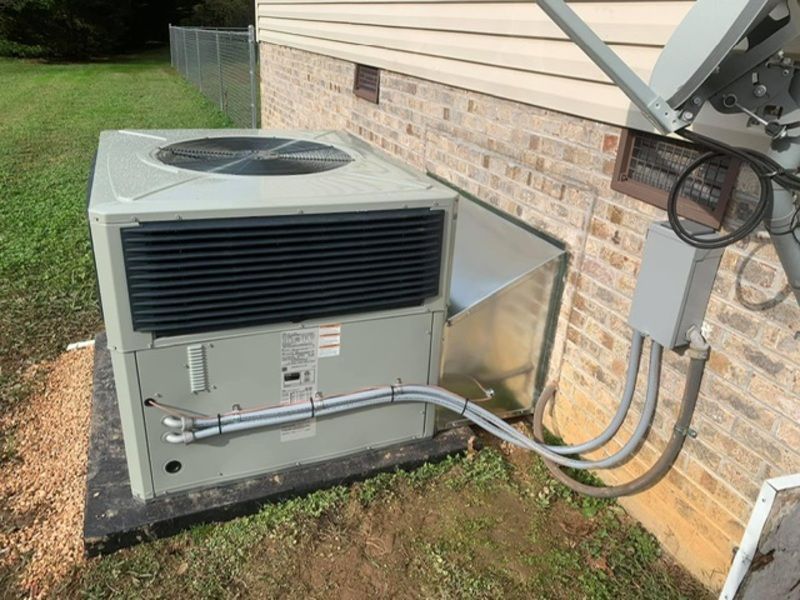 Outdoor air conditioning unit beside a house wall with connected electrical conduit and tubing