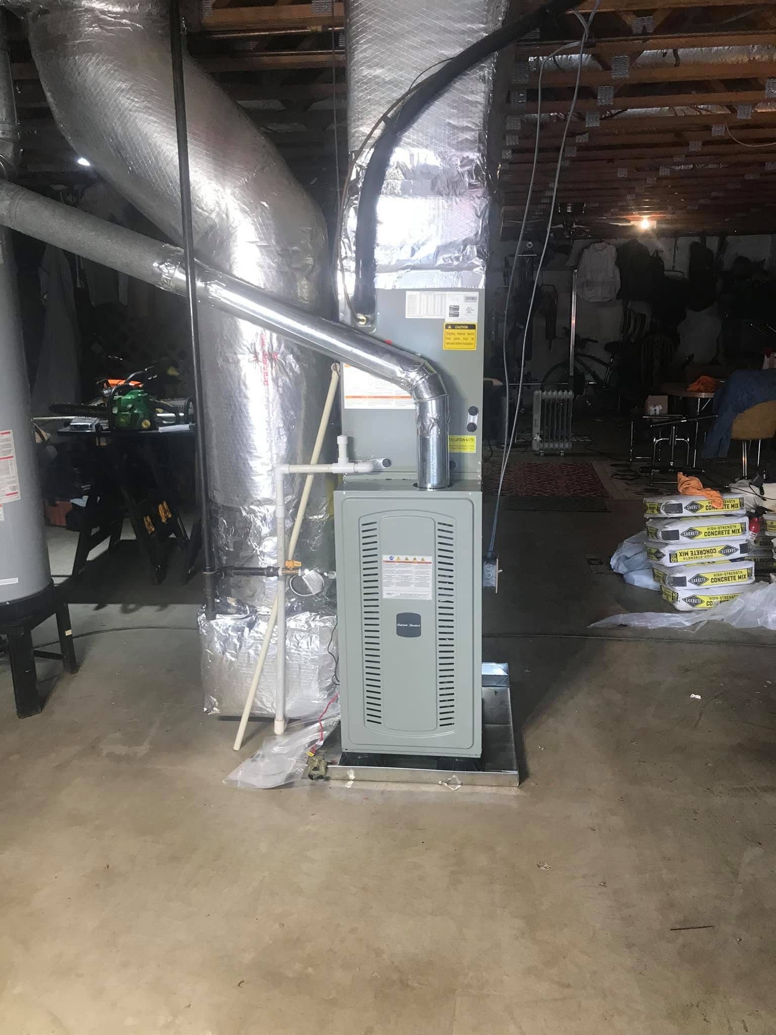 Large HVAC unit with silver ductwork in an unfinished basement or utility room.