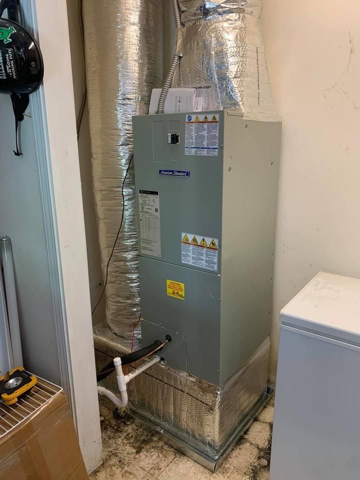 Gray HVAC furnace in a utility closet with silver ductwork and a wall thermostat nearby