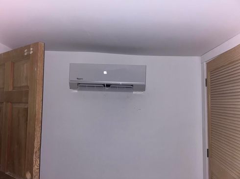 Wall-mounted air conditioner centered on a light gray room wall, with wooden doors on both sides.