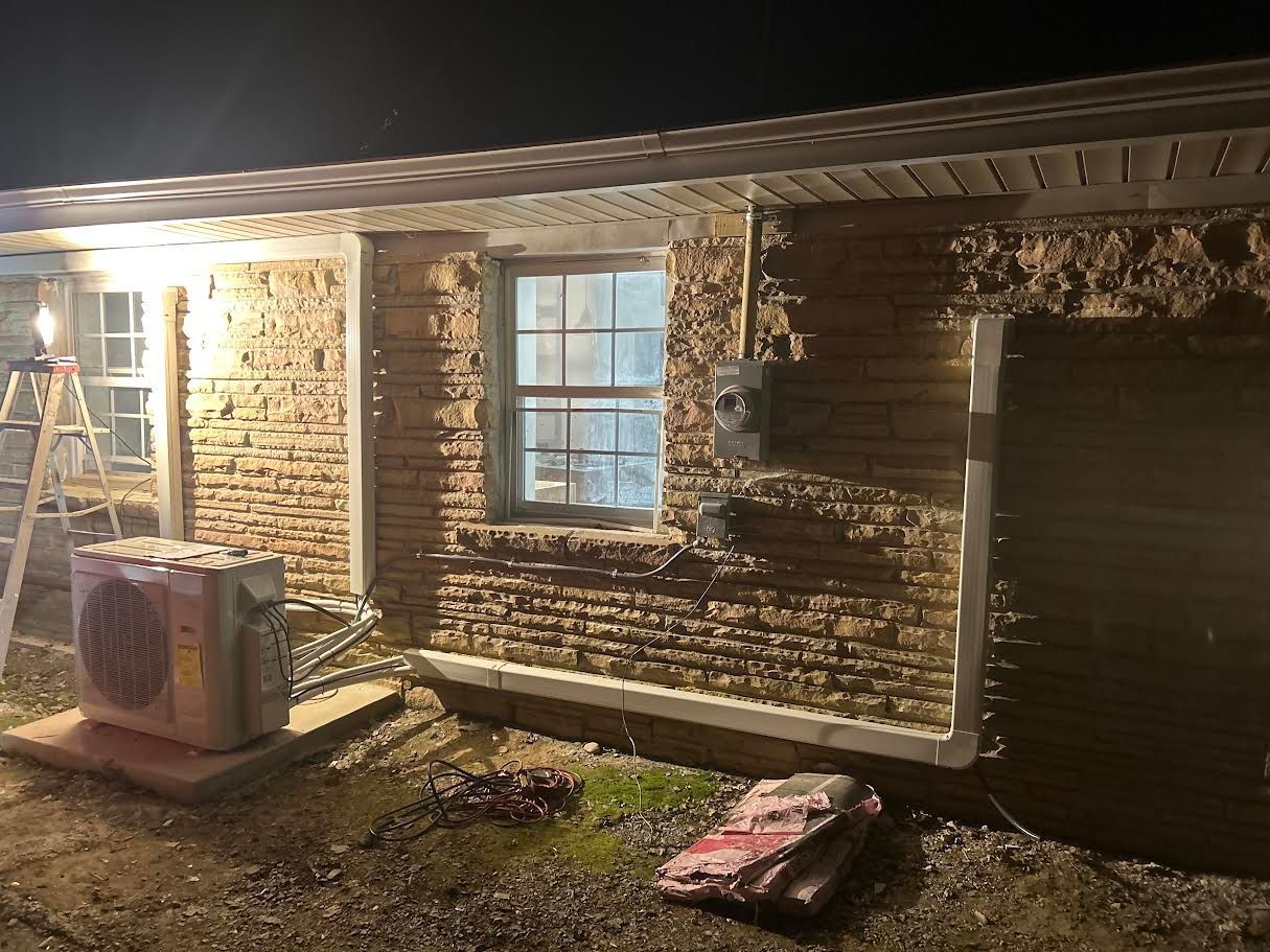 Nighttime view of a brick house exterior with lit windows, a garage door, and a ladder leaning near the porch