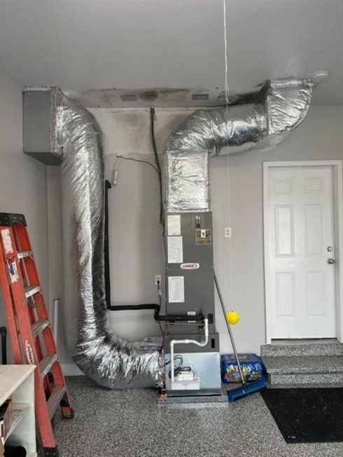 Basement HVAC system with silver ductwork, furnace, ladder, and a white door near a carpeted entryway