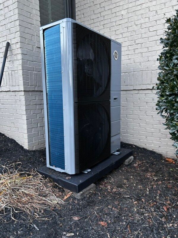 Outdoor HVAC unit beside a brick building, with blue and black panels on a concrete pad.