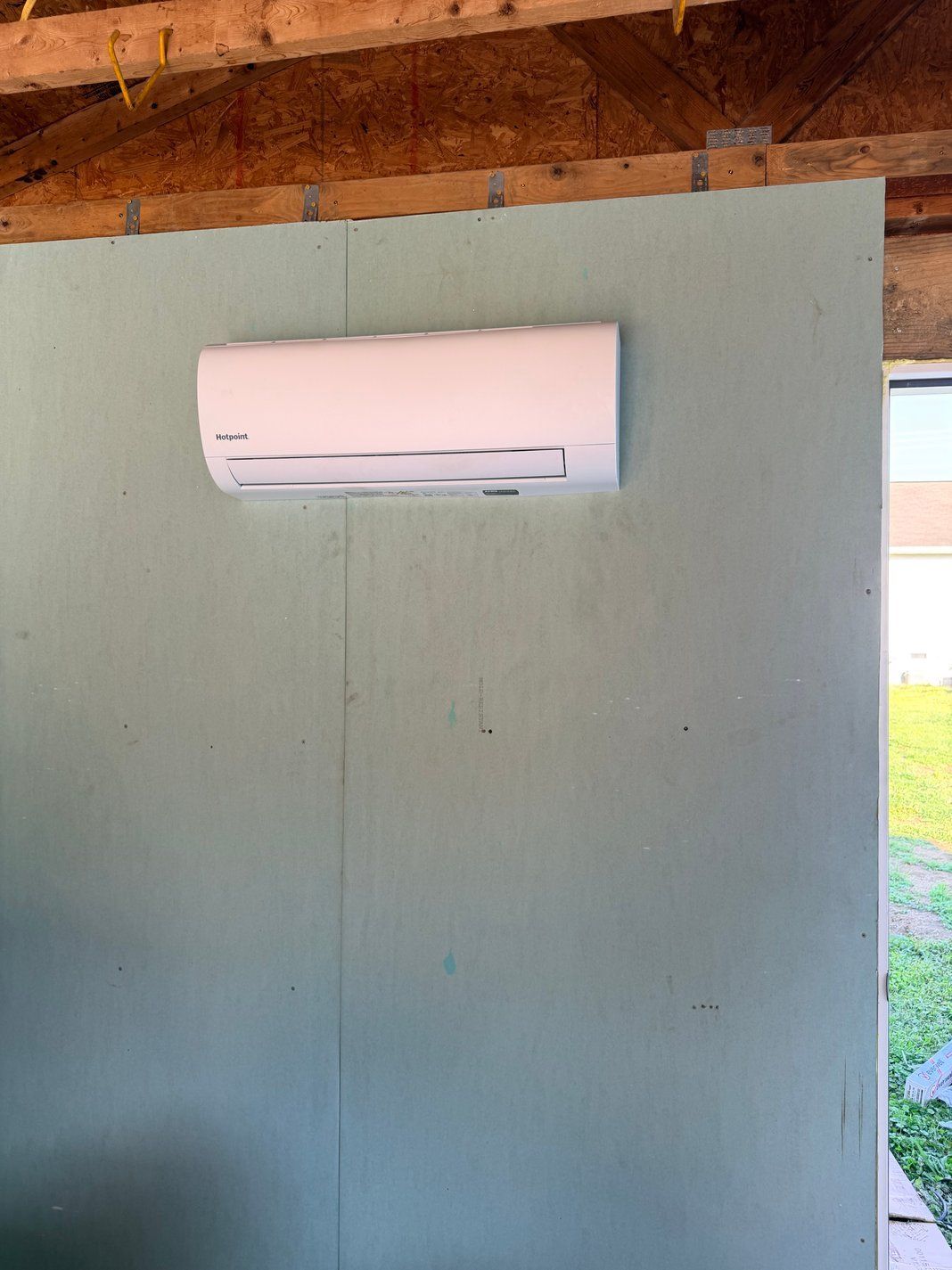 White wall-mounted air conditioner on a pale green wall under exposed wooden beams.