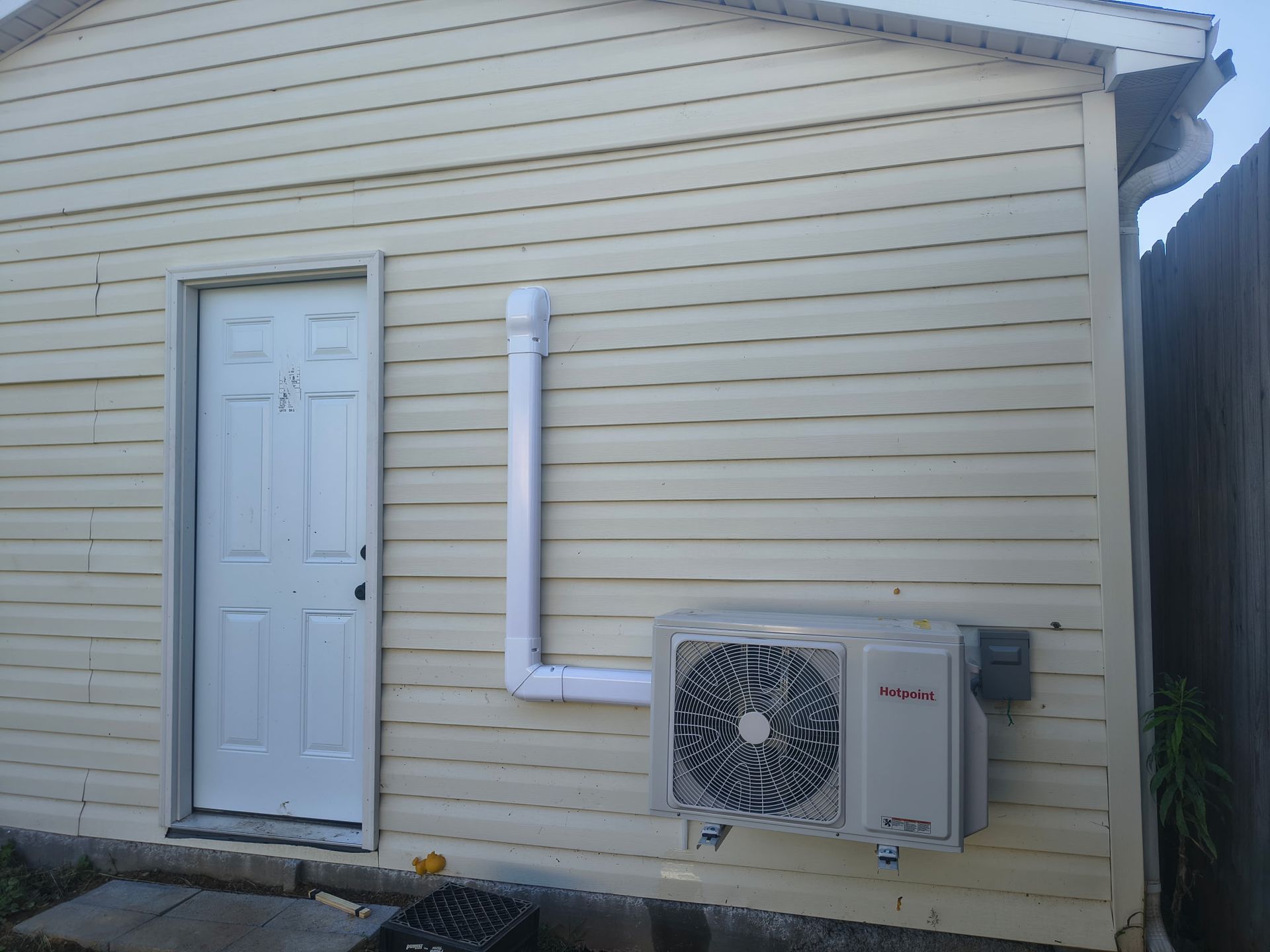 Side of a beige house with a white door and wall-mounted air conditioner unit