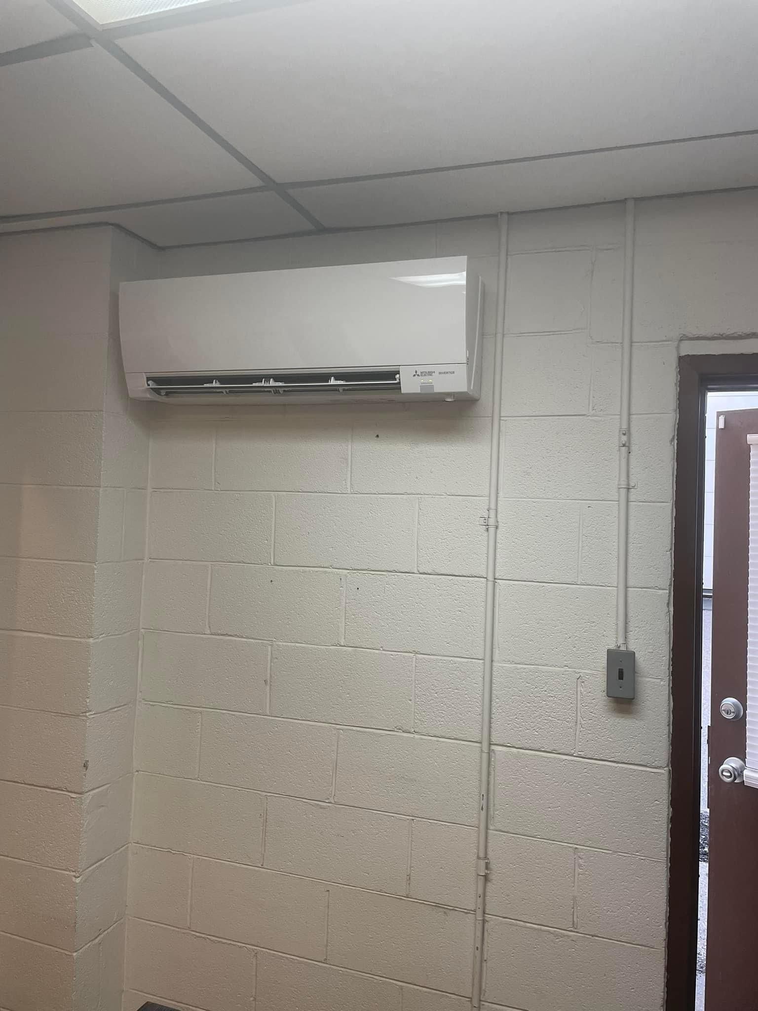 Wall-mounted air conditioner above a cinderblock wall near a doorway in a plain room