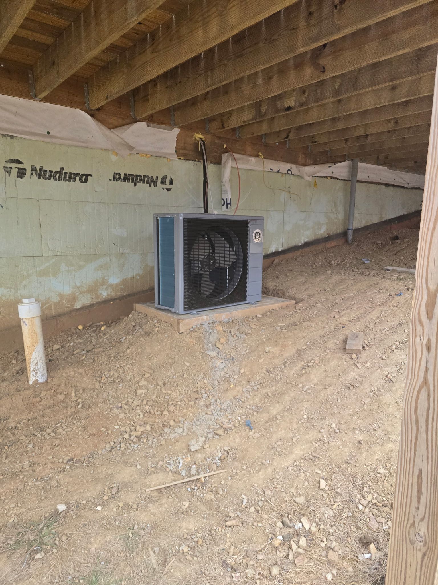 Small blue box fan under a low wooden roof in a dusty, unfinished crawlspace