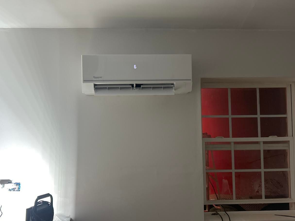 Wall-mounted air conditioner above a window with red light shining through the panes.