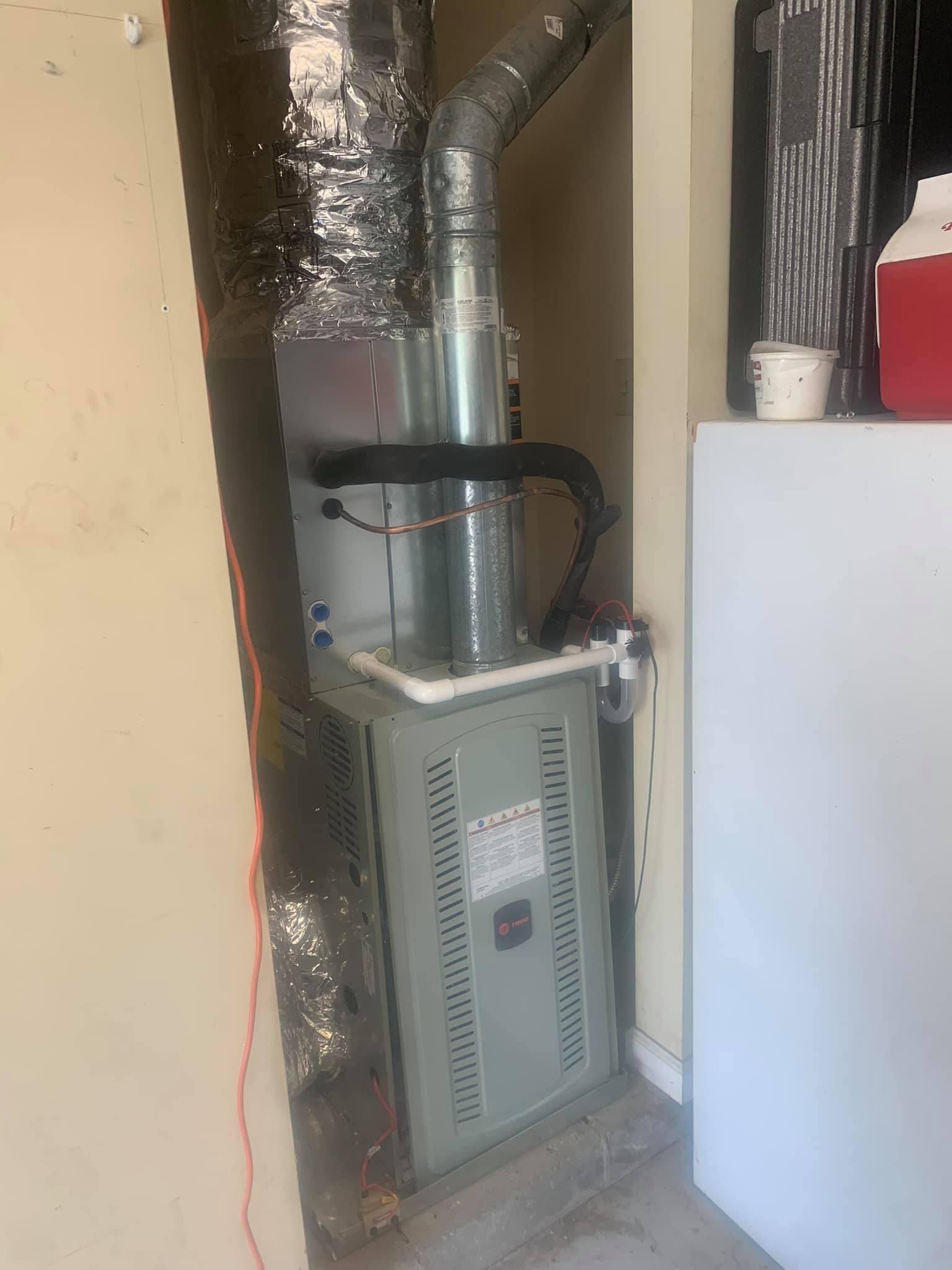 Gas furnace in a utility closet with silver ductwork and a white water heater.