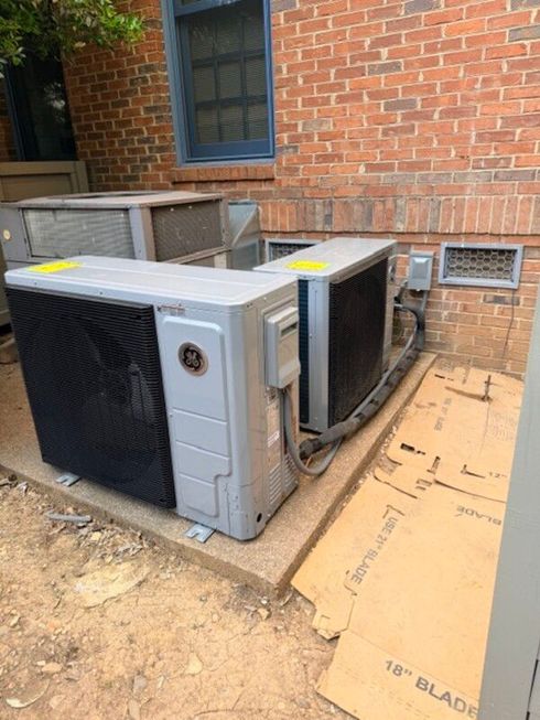 Two outdoor HVAC units beside a brick building, one panel open and exposed.