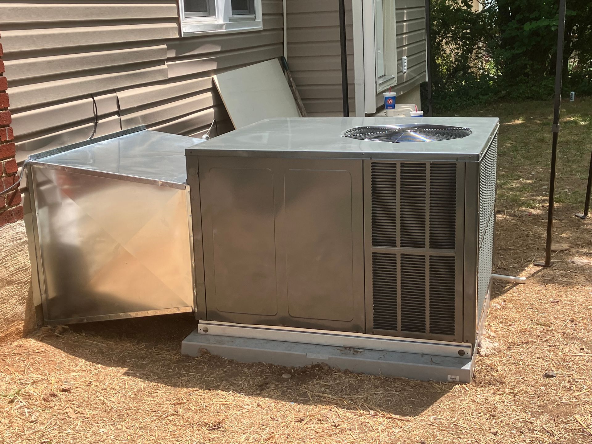 Two large metal HVAC units beside a house on a gravel yard.