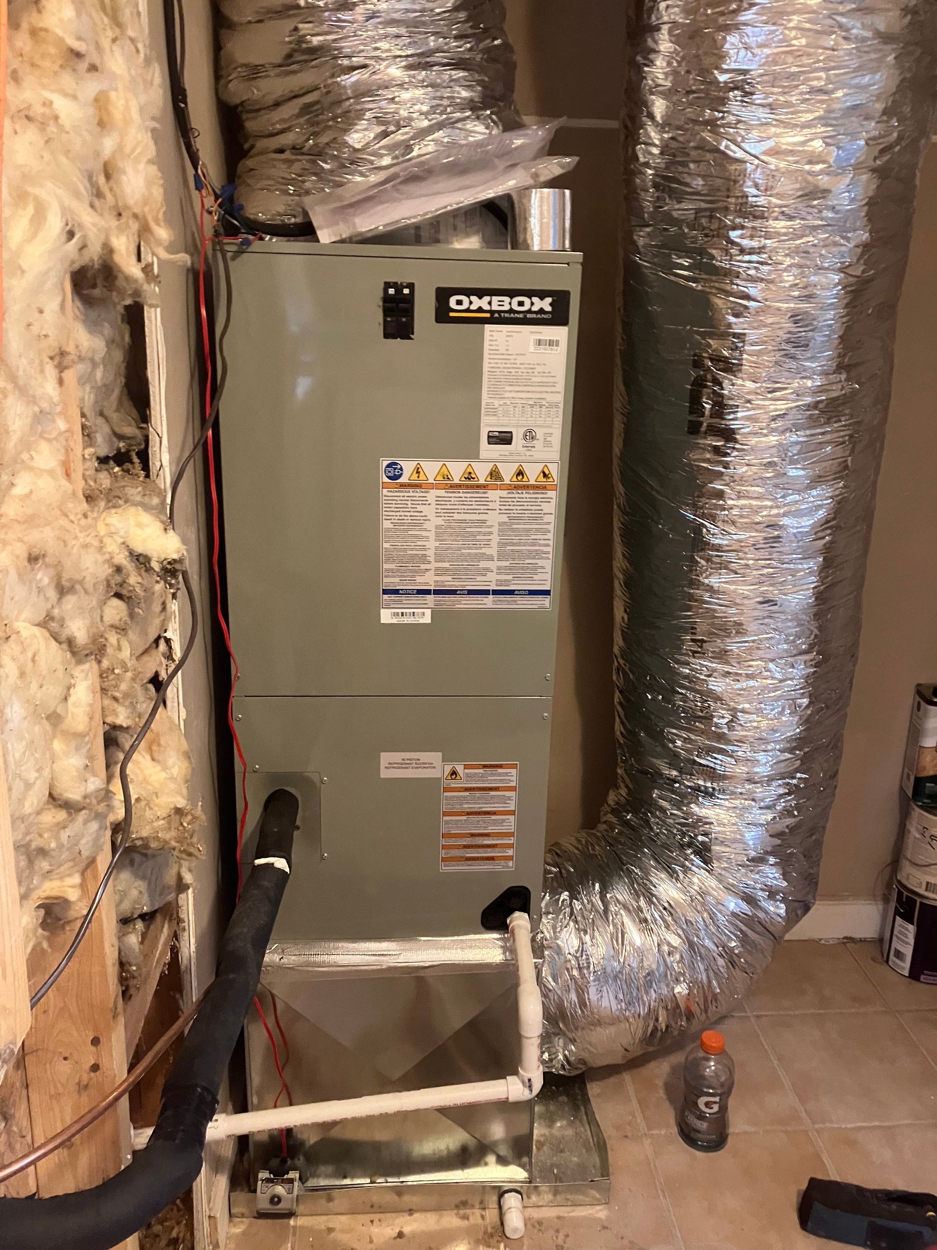 Furnace unit in a basement utility area, surrounded by insulated ductwork and exposed wall insulation.