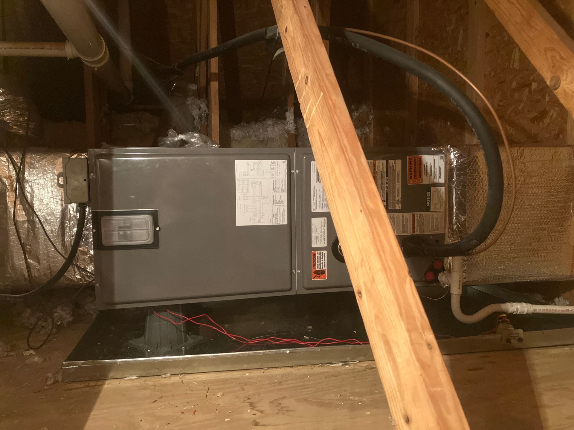 HVAC unit in an unfinished attic, partly blocked by a wooden beam and wiring.