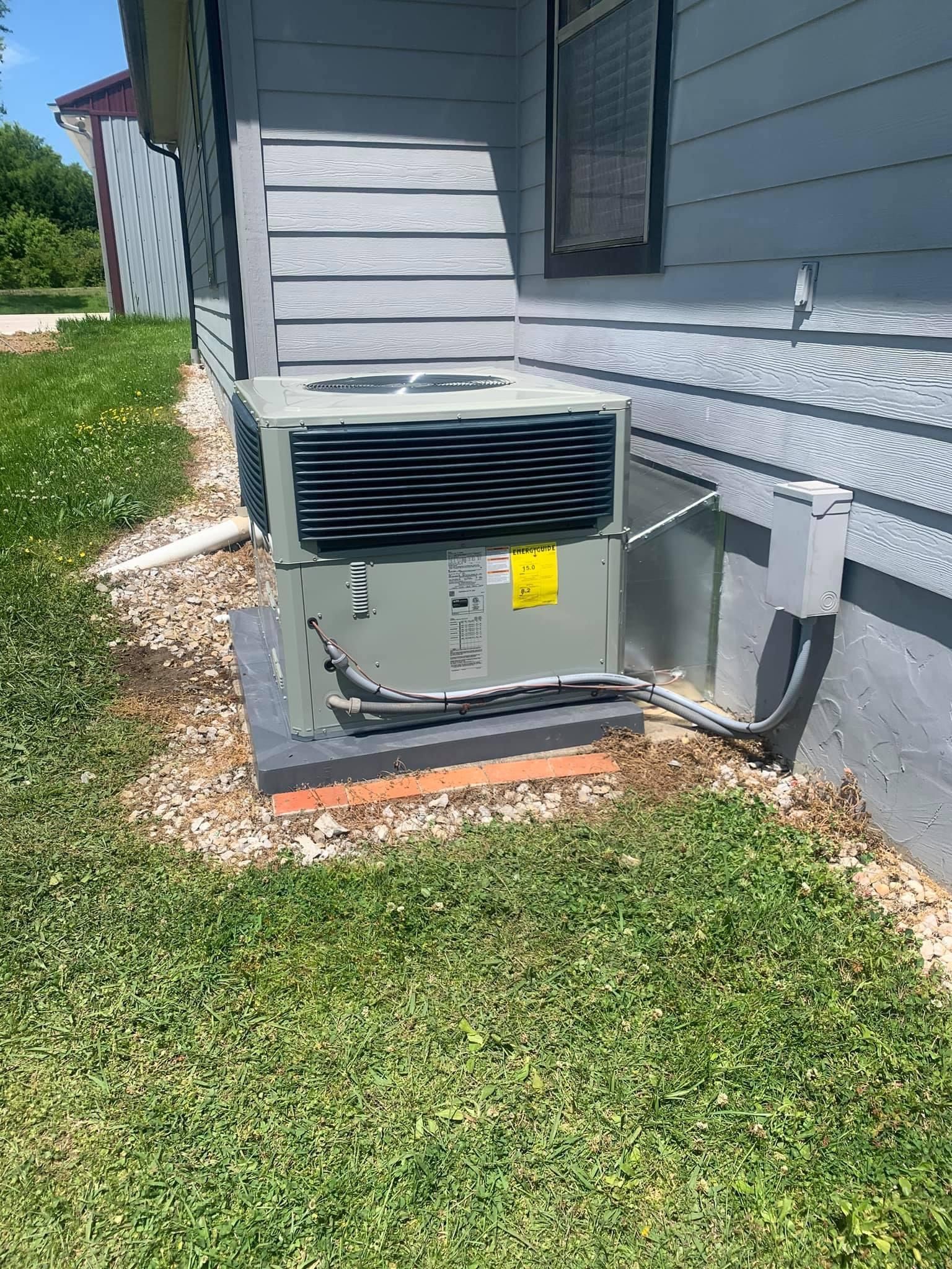 Outdoor HVAC unit beside a gray house with white trim and grass in the foreground