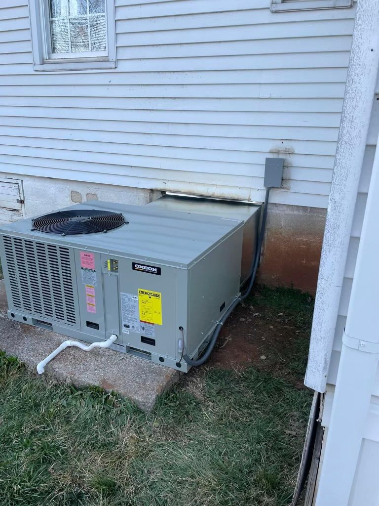 Outdoor HVAC unit beside a house with white siding, sitting on grass and a concrete pad.
