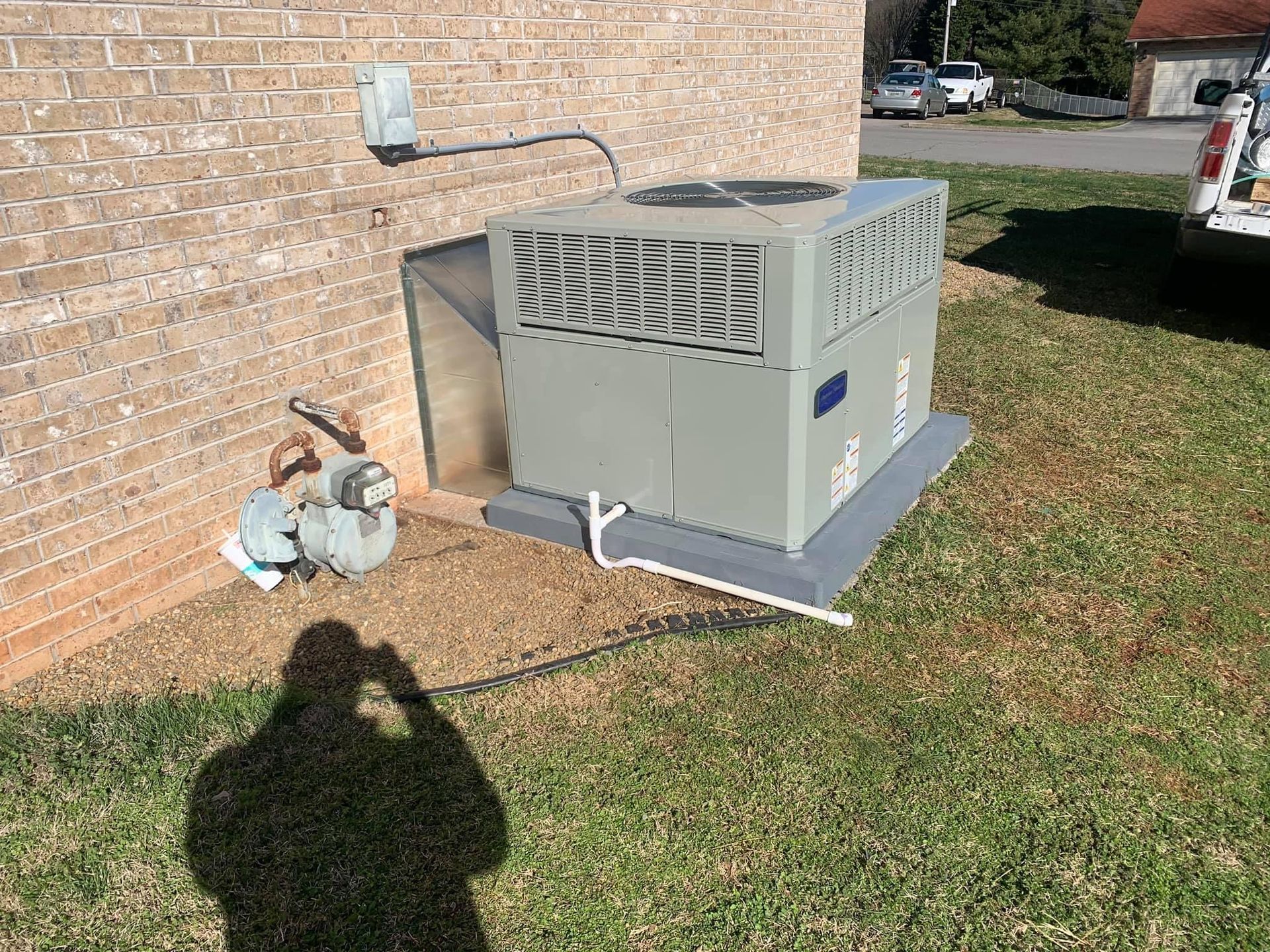 Outdoor HVAC unit beside a brick house, with gas meter and grassy yard.
