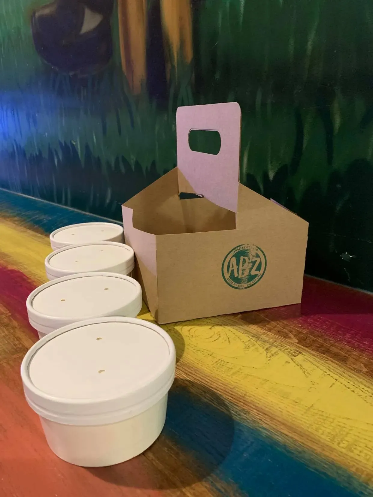 Four white take-out cups arranged in a line next to a cardboard carrier with the