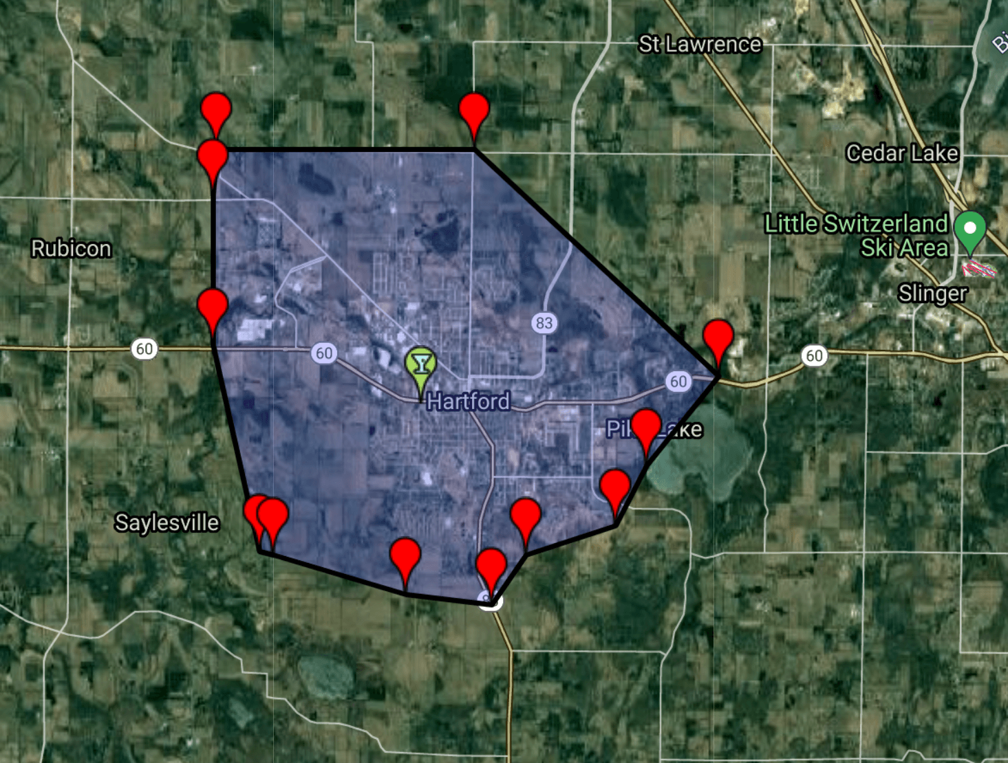 A satellite map view showing a blue-shaded, polygon-shaped area marked with red pins around a central location.