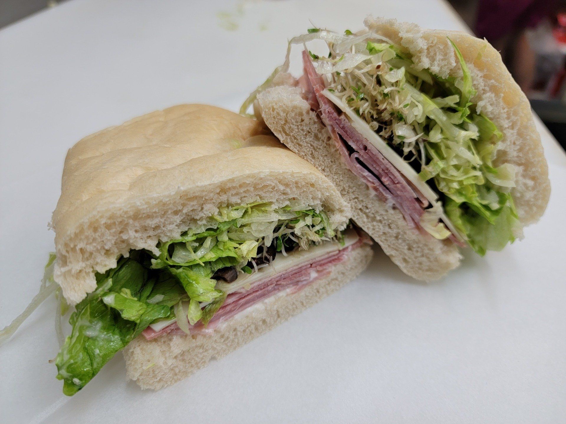 Two halves of a ham and cheese sandwich with lettuce on a white surface.