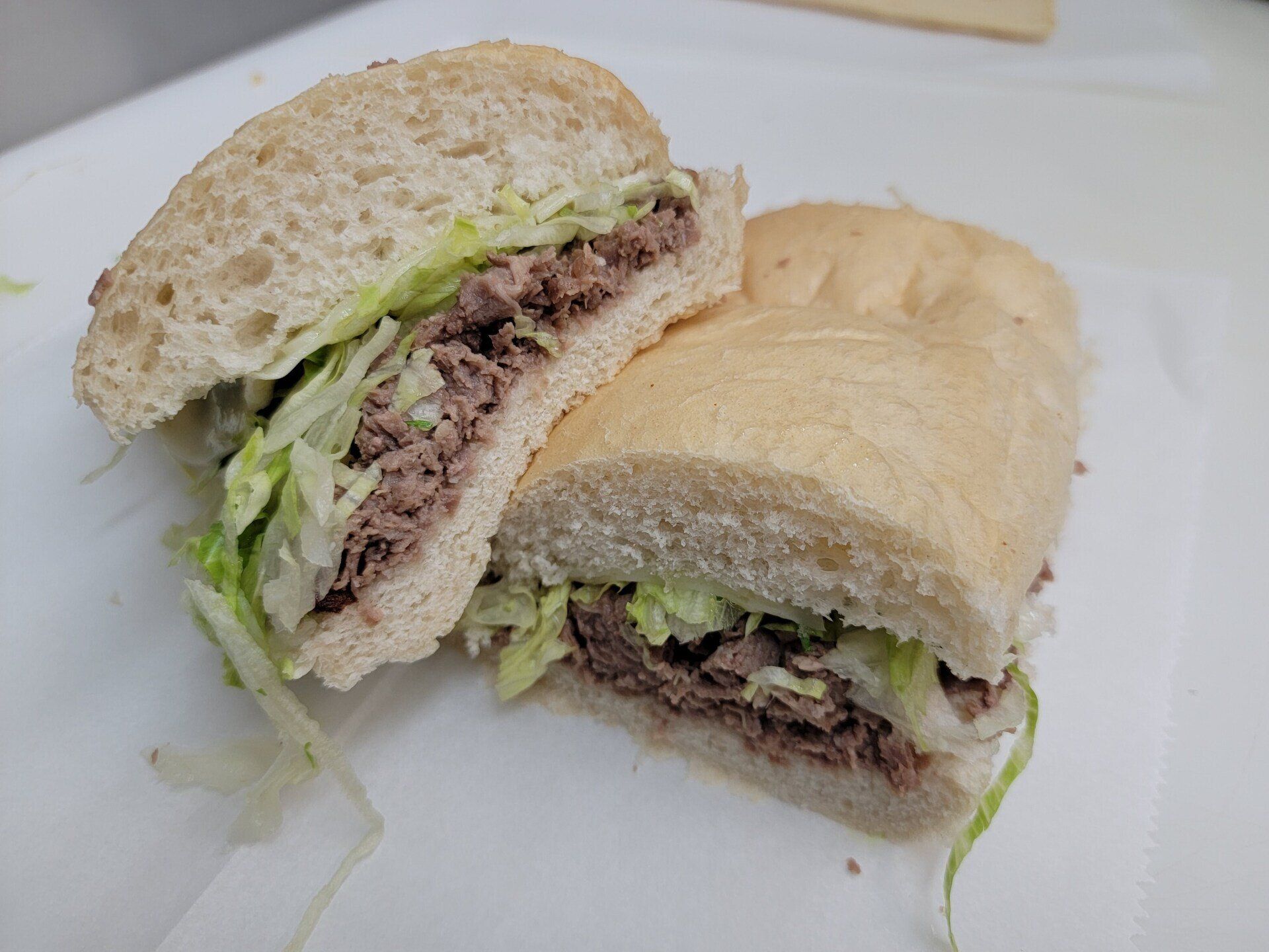 A sandwich cut in half on a white surface, featuring roast beef and shredded lettuce on a soft, light-colored roll.