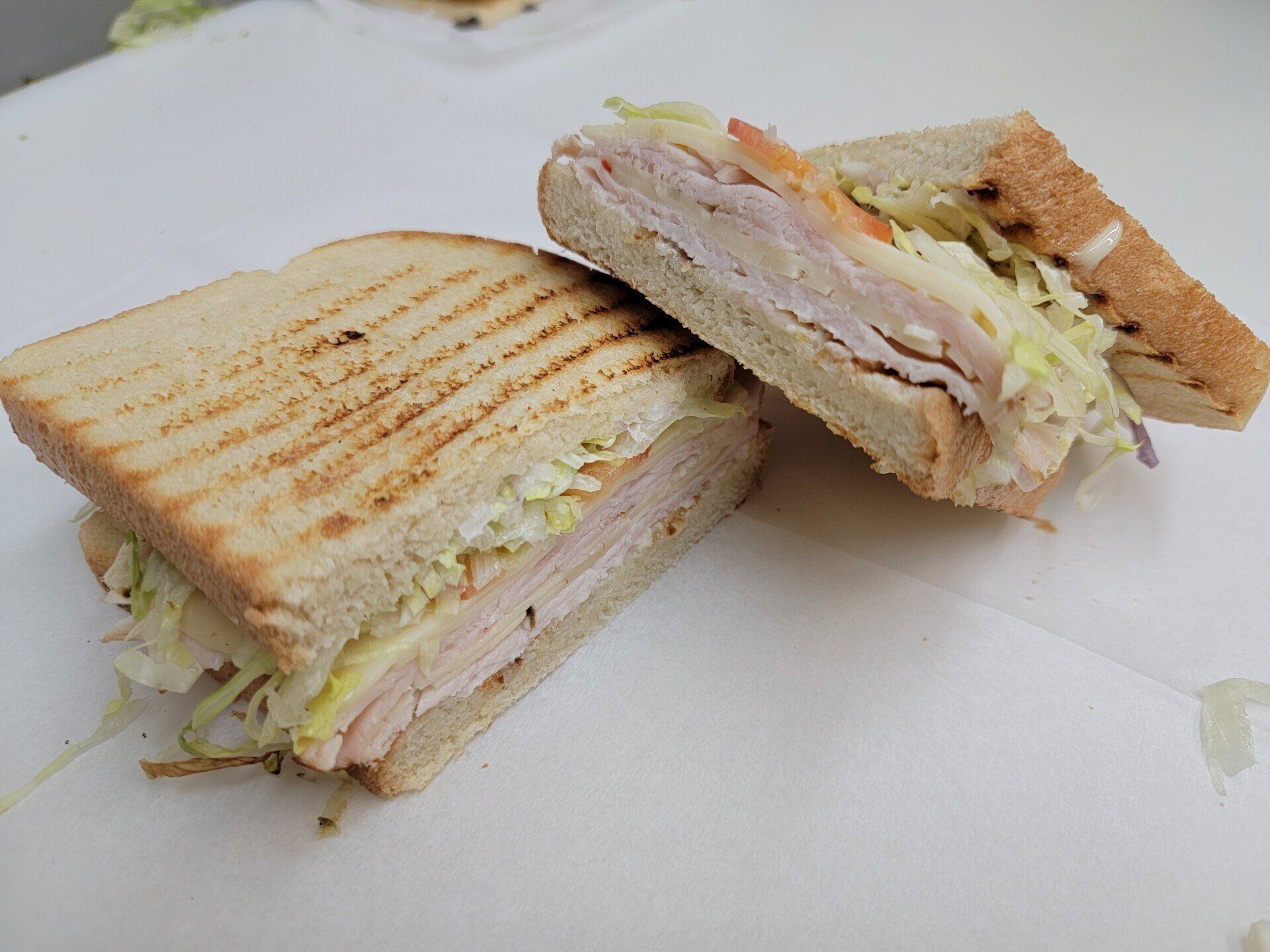Two halves of a toasted ham and shredded lettuce sandwich on a white surface.