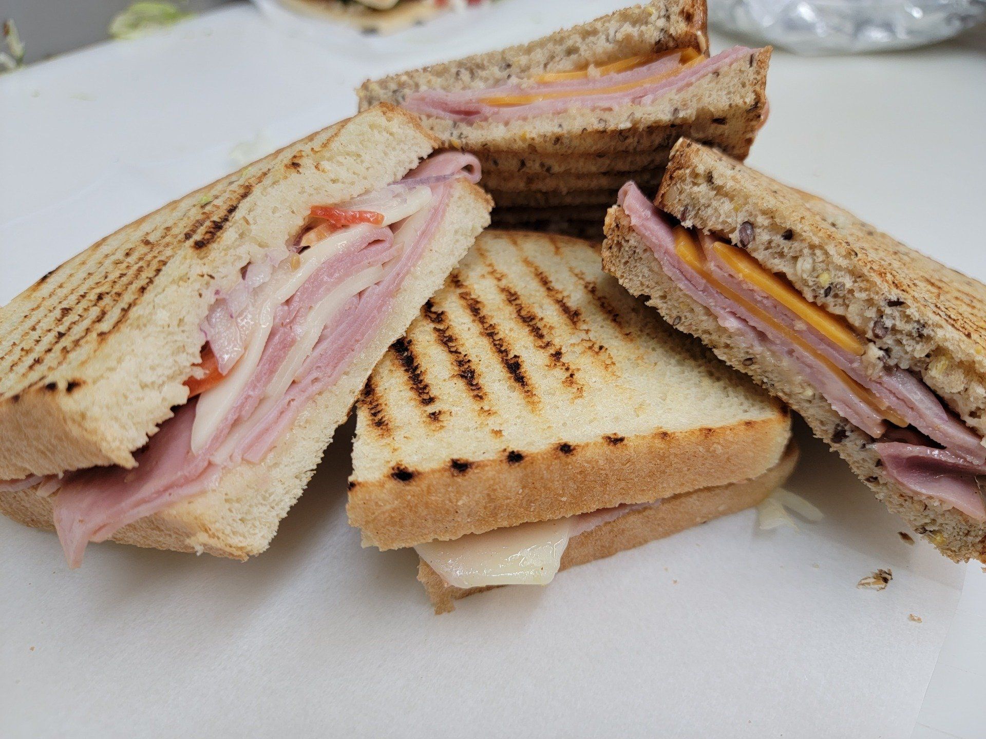 A group of toasted ham and cheese sandwiches arranged on a white surface.