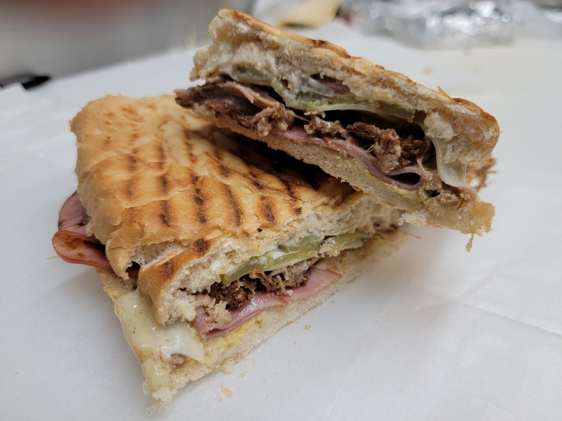 A grilled Cuban sandwich cut in half, showing layers of ham, roasted pork, melted cheese, and pickles on pressed bread.