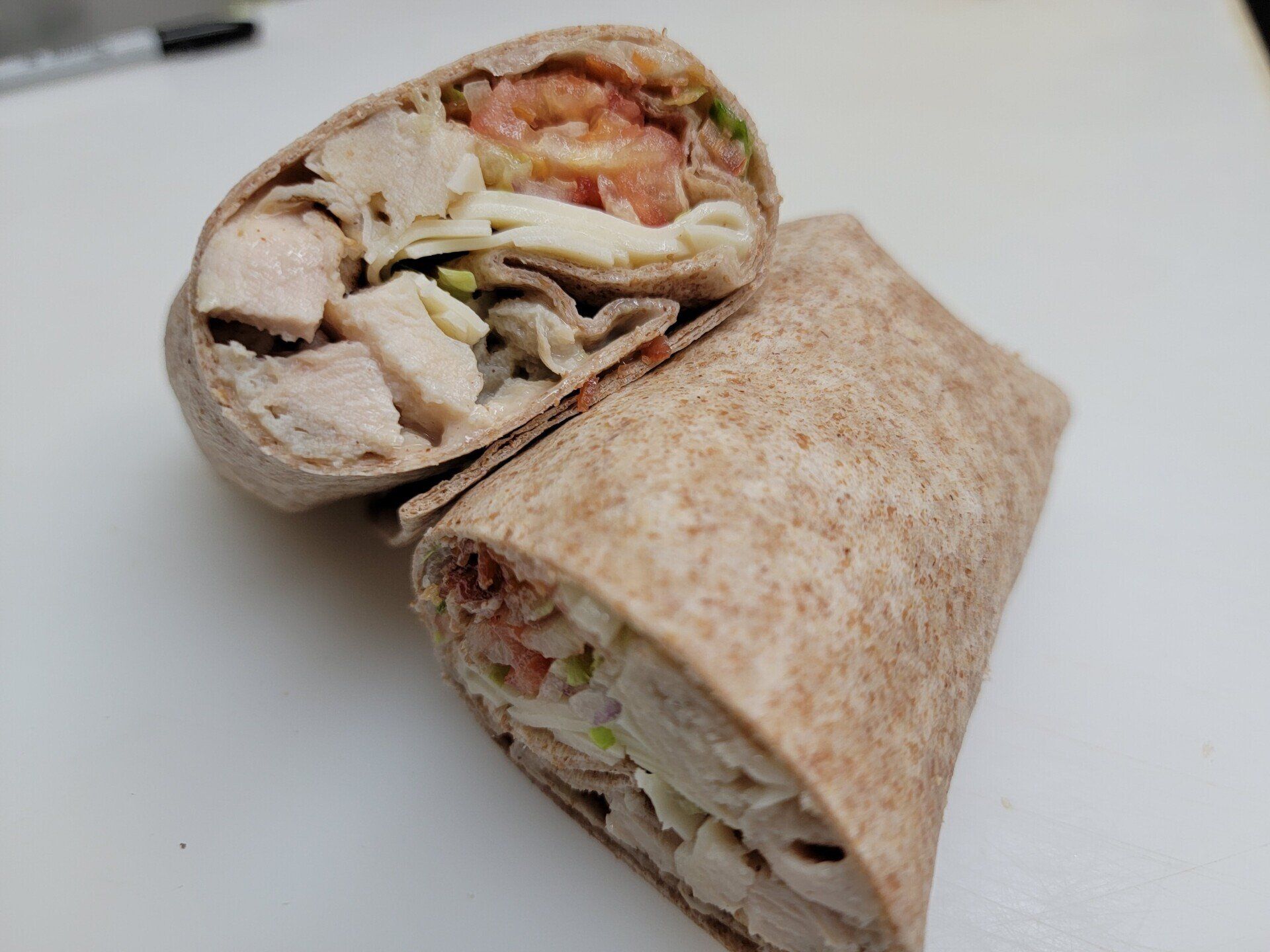 A sliced whole wheat wrap filled with diced chicken, cheese, and diced tomatoes on a white surface.