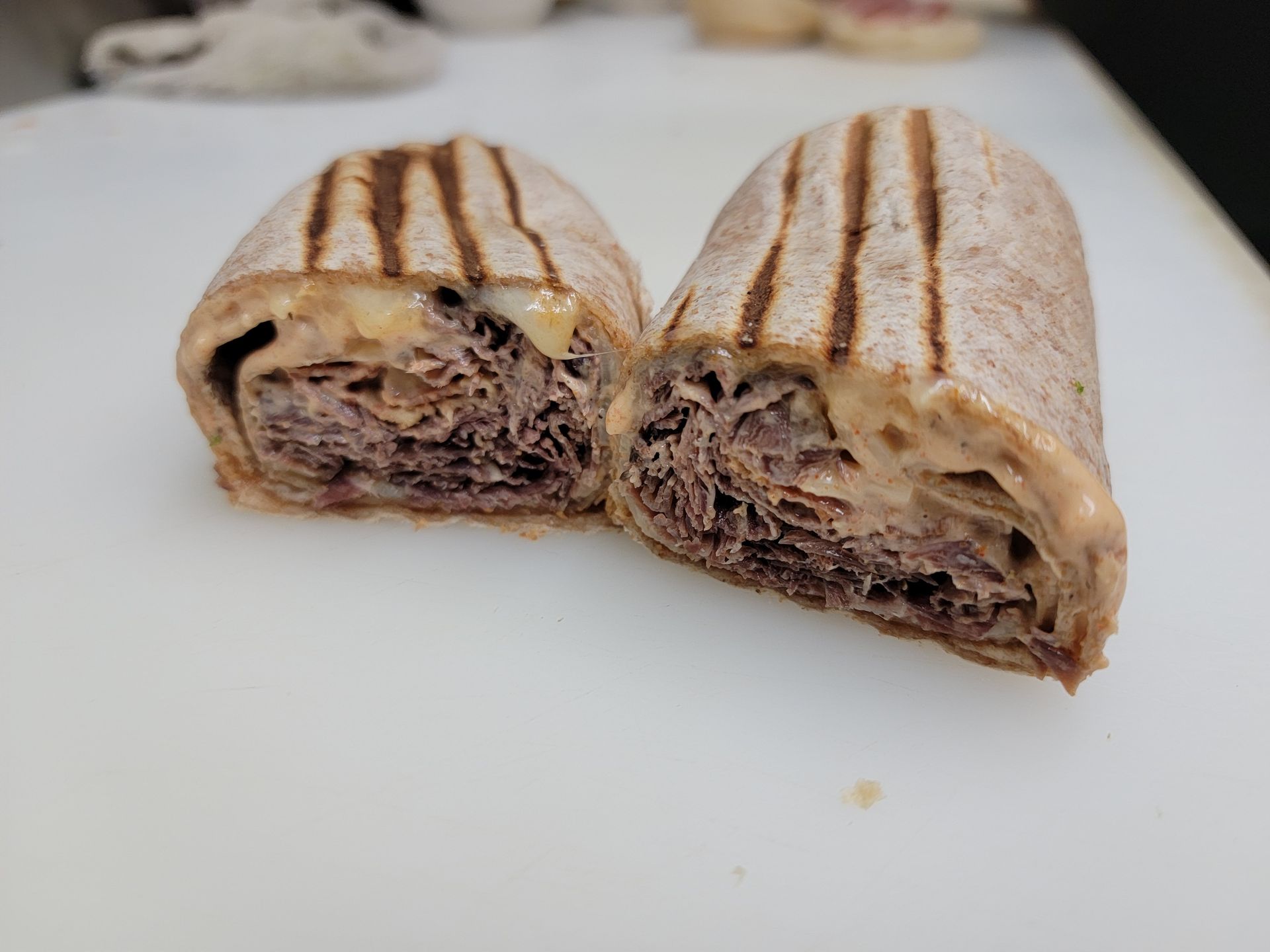Two halves of a grilled whole-wheat wrap filled with sliced roast beef and melted cheese on a white cutting board.
