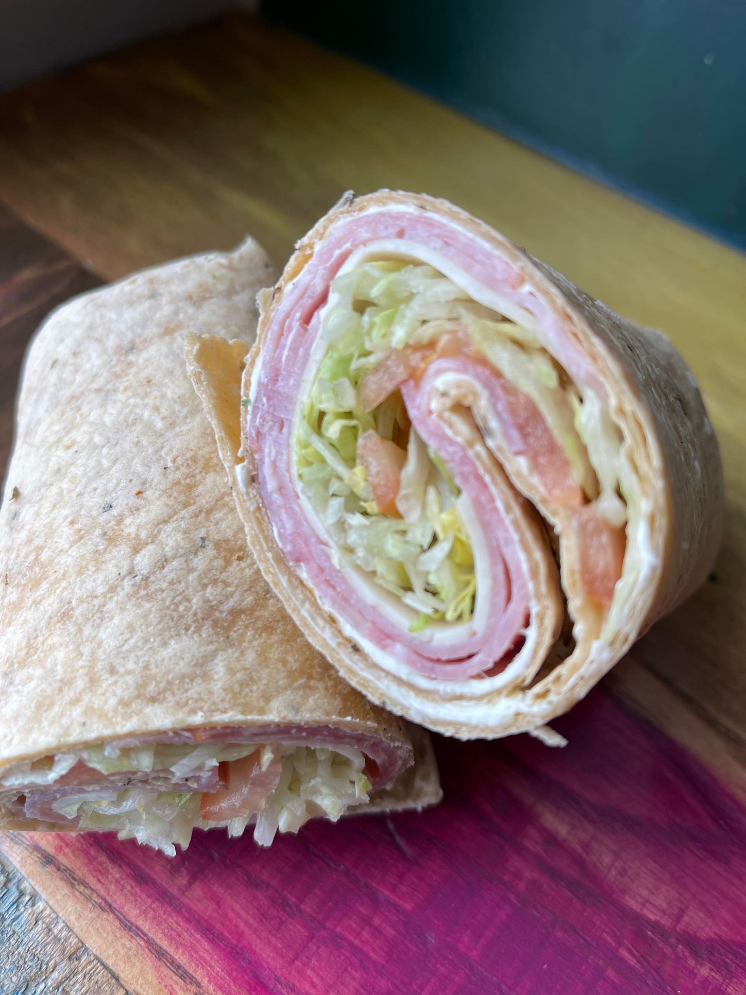 A sliced wrap with ham, cheese, shredded lettuce, and tomato on a wooden cutting board.