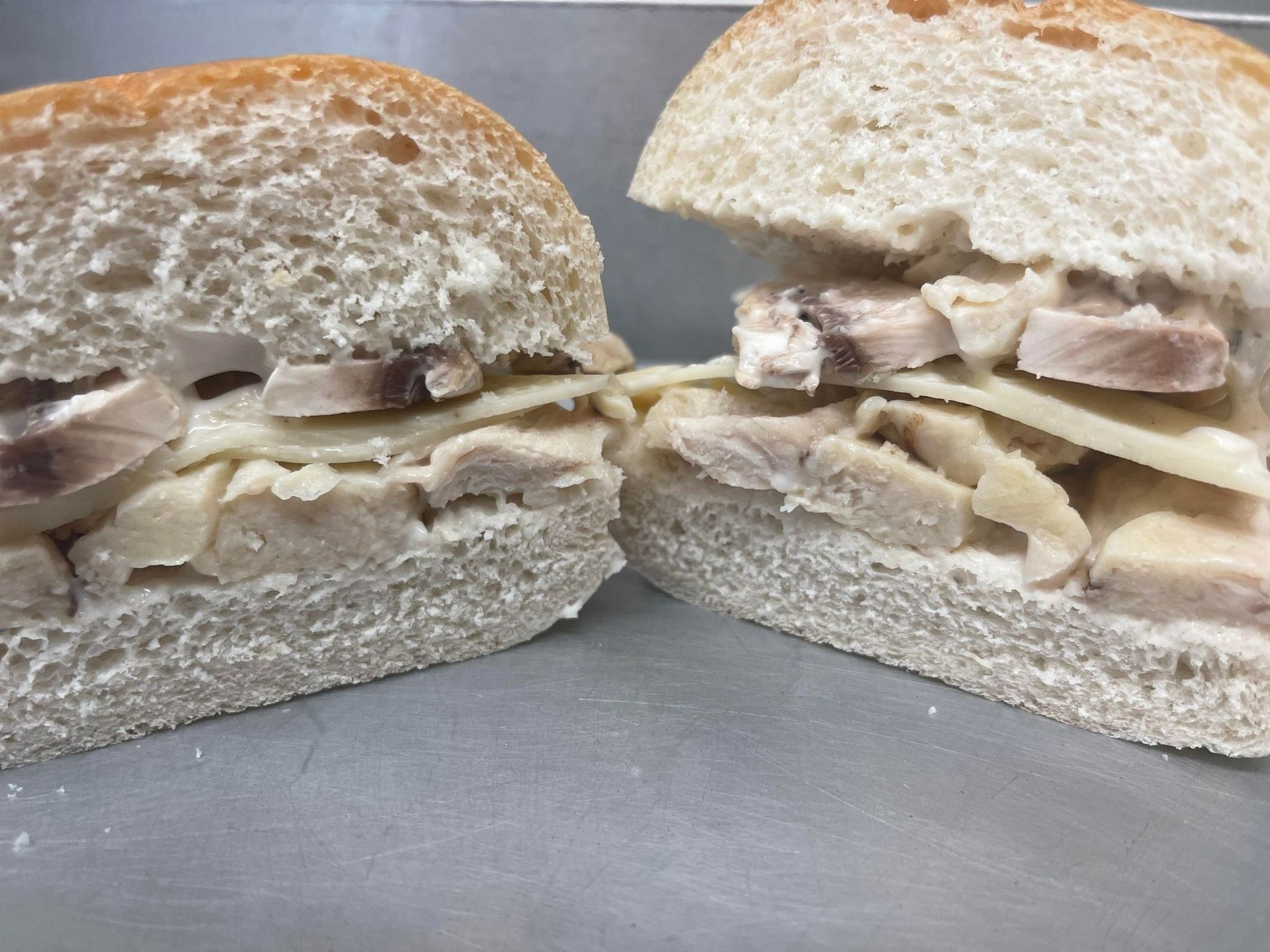 A split sandwich on rustic bread, filled with sliced poultry, melted white cheese, and sliced mushrooms.
