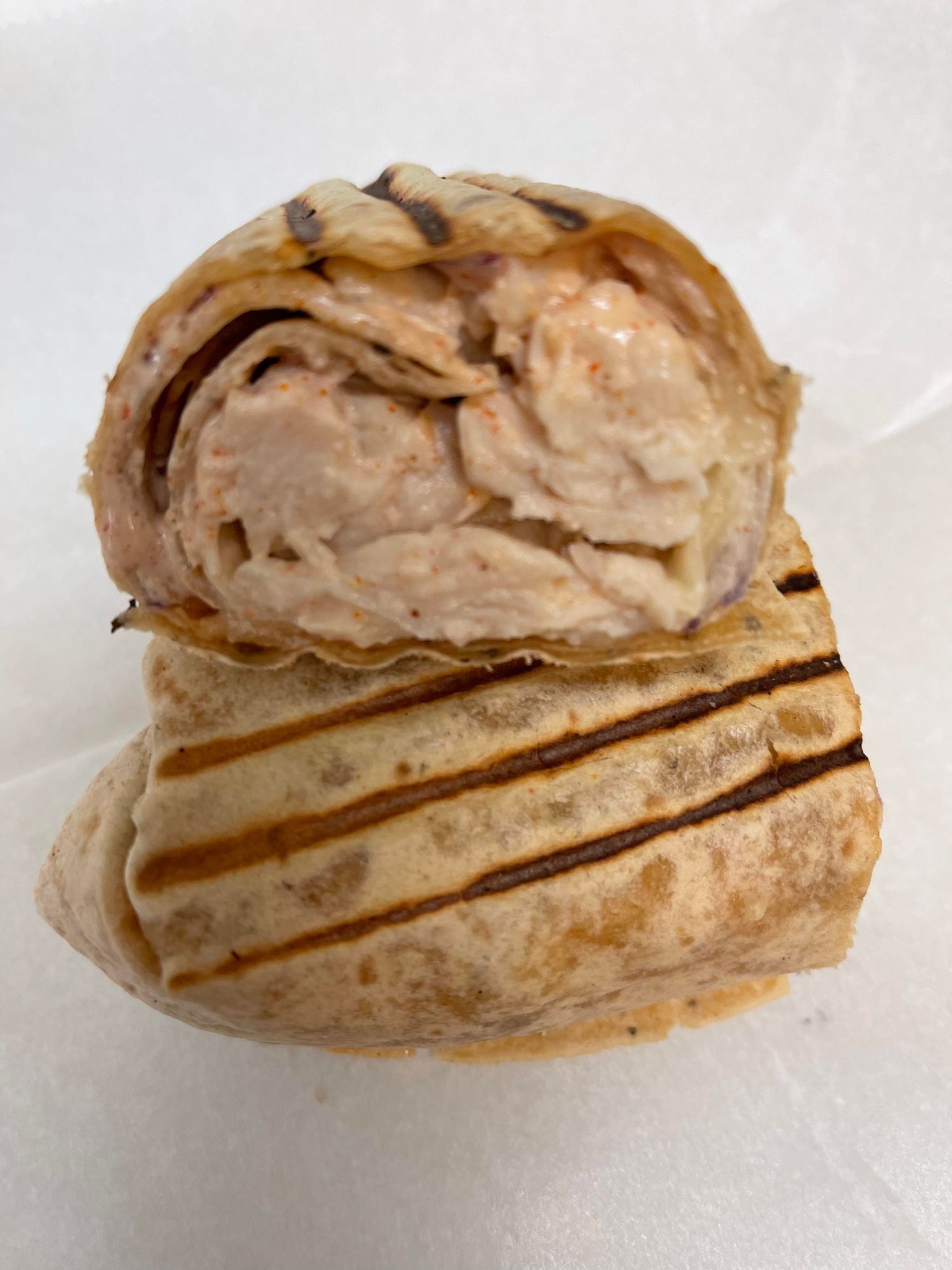 A toasted tortilla wrap sliced in half, showing a creamy, light-colored chicken filling inside.
