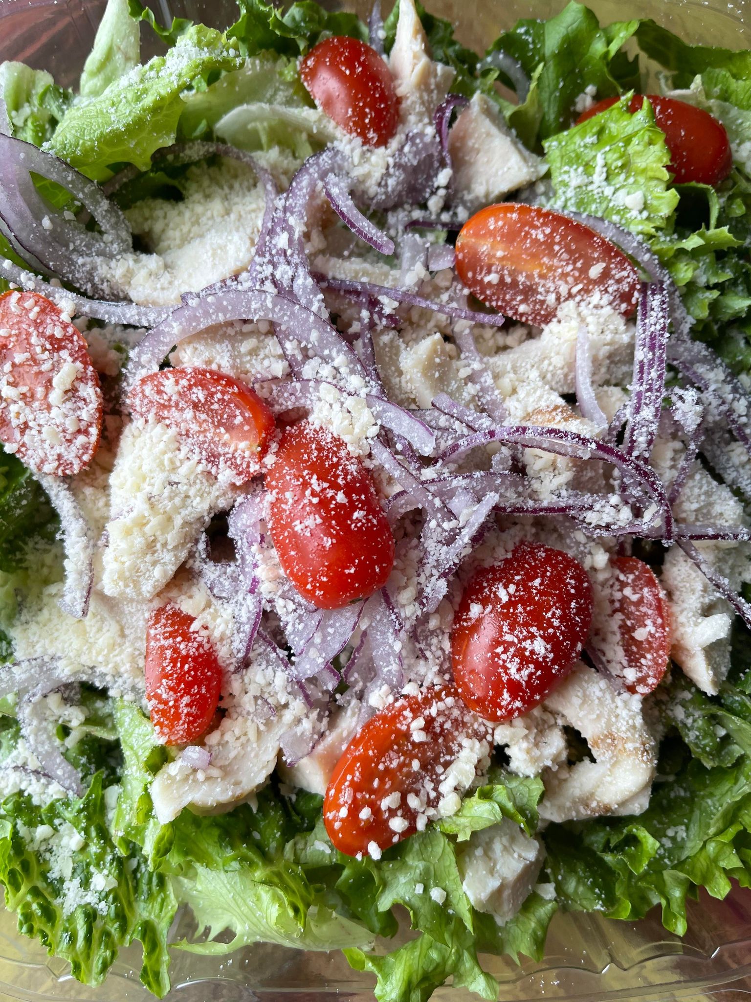 A crisp salad with green lettuce, sliced red onion, halved cherry tomatoes, and grilled chicken sprinkled with cheese.