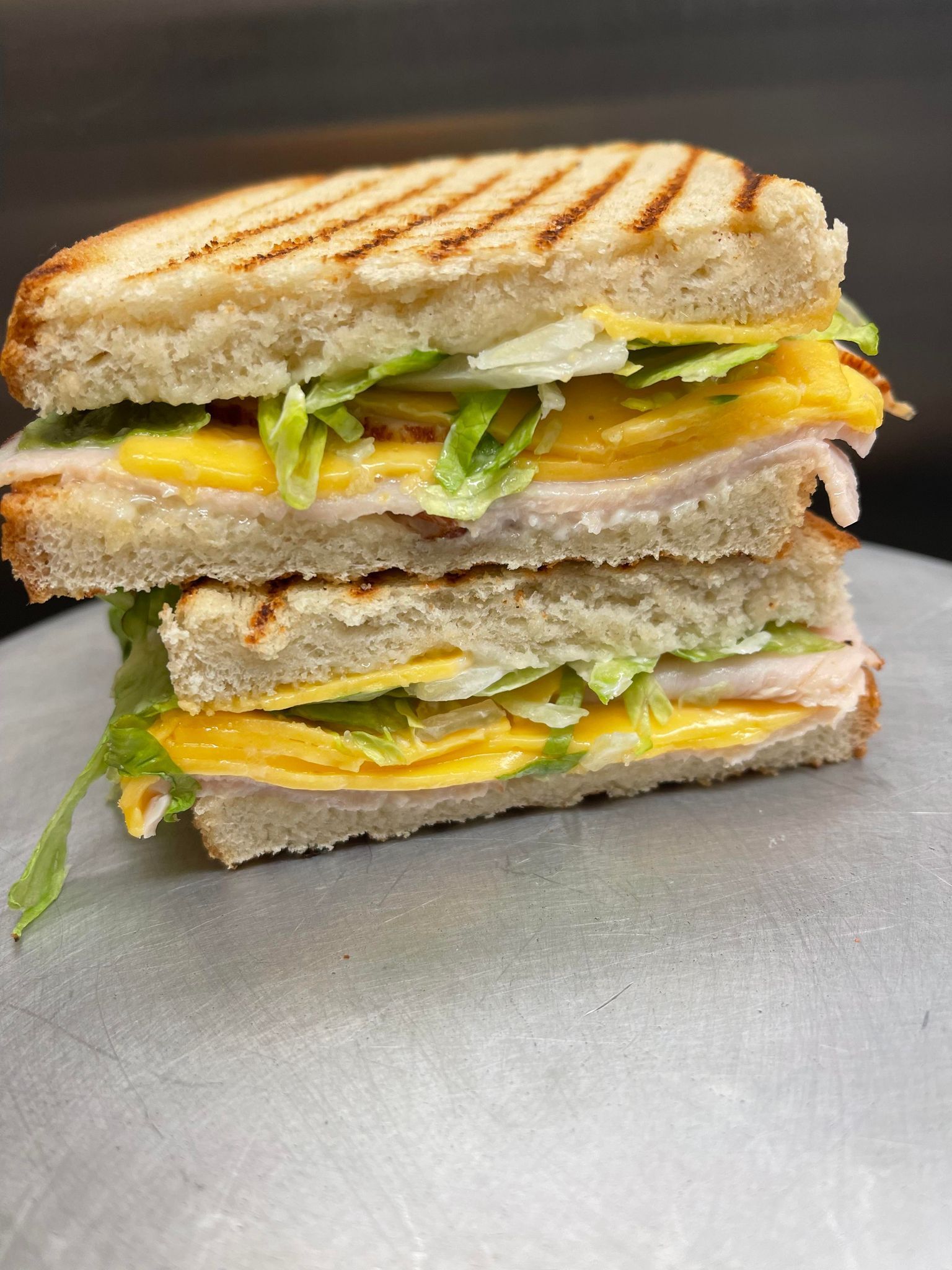A stacked, grilled turkey and cheese sandwich with lettuce on toasted, griddle-marked bread, set on a metal surface.