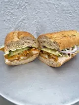 Two halves of a toasted sub sandwich featuring meat, pickles, and red onion, resting on a silver metal tray.