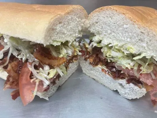 A halved BLT sub sandwich featuring crispy bacon, shredded lettuce, and sliced tomato on a soft, light-colored roll.