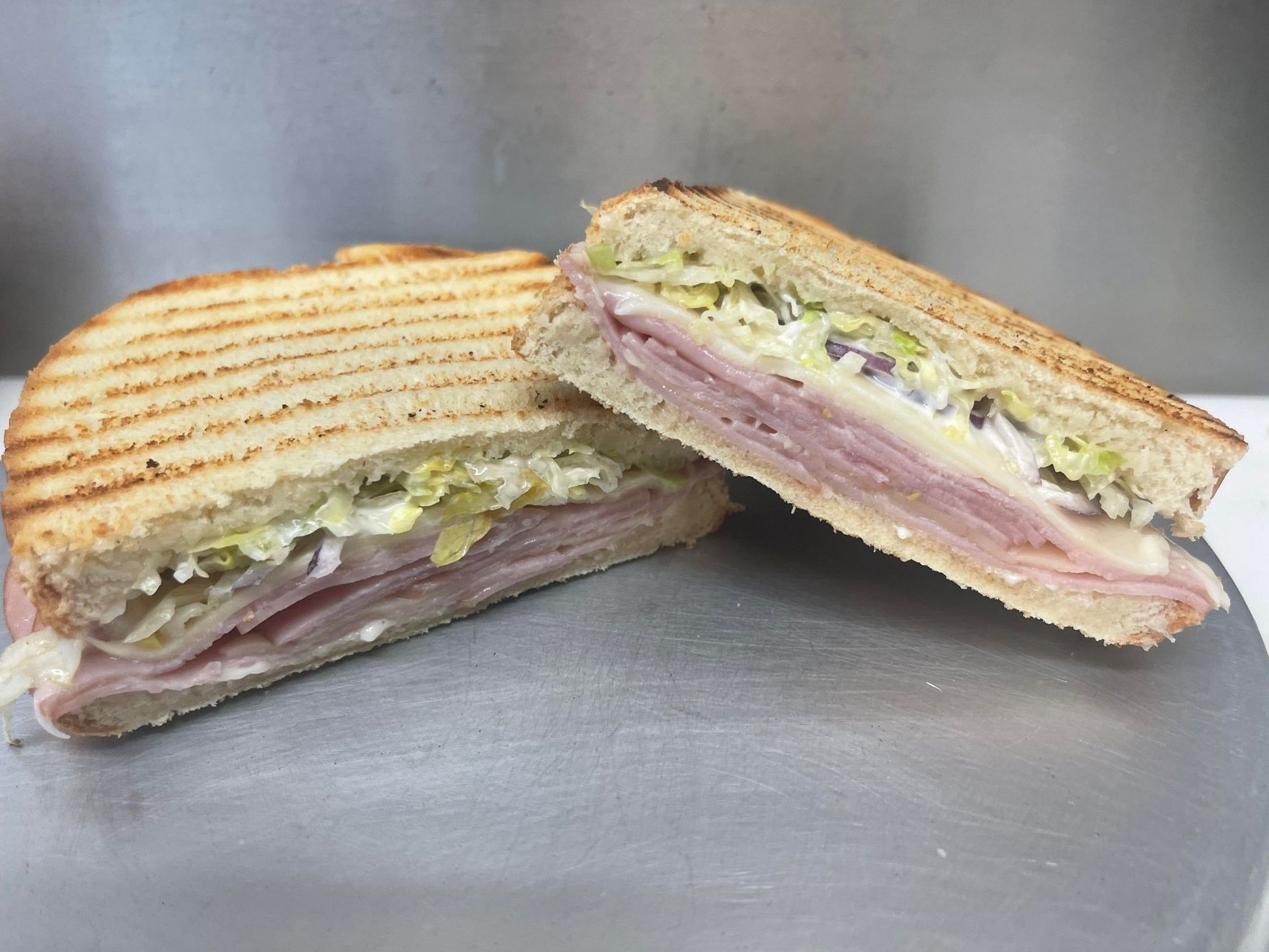 Two halves of a toasted ham and cheese panini with shredded lettuce and relish filling on a metallic surface.