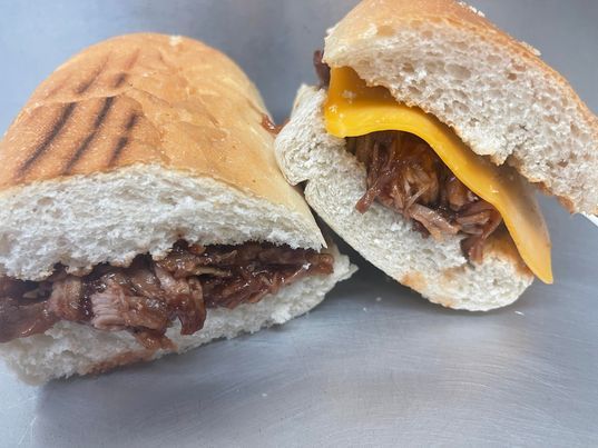 Two halves of a toasted sub sandwich filled with shredded meat and a slice of yellow cheese on a metallic surface.