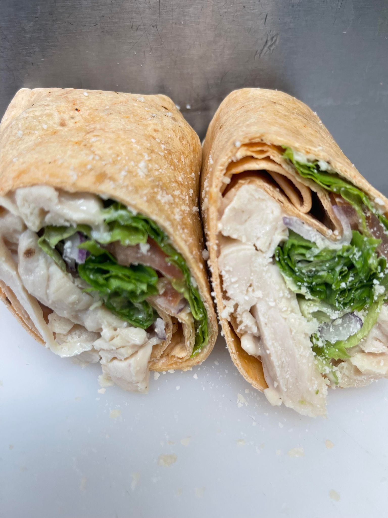 Two halves of a chicken Caesar wrap cut diagonally, showing chicken, lettuce, and dressing in a light-brown tortilla.