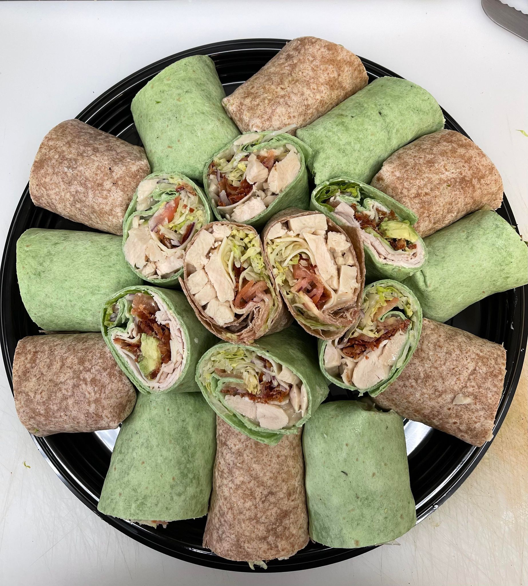 A platter containing an assortment of sliced green spinach and brown whole wheat chicken wraps arranged in a circle.