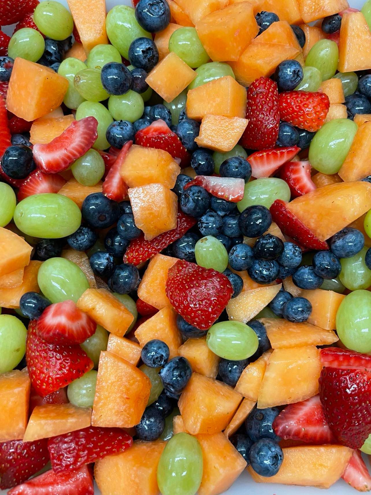 A colorful fruit salad with cantaloupe chunks, fresh blueberries, green grapes, and sliced strawberries.