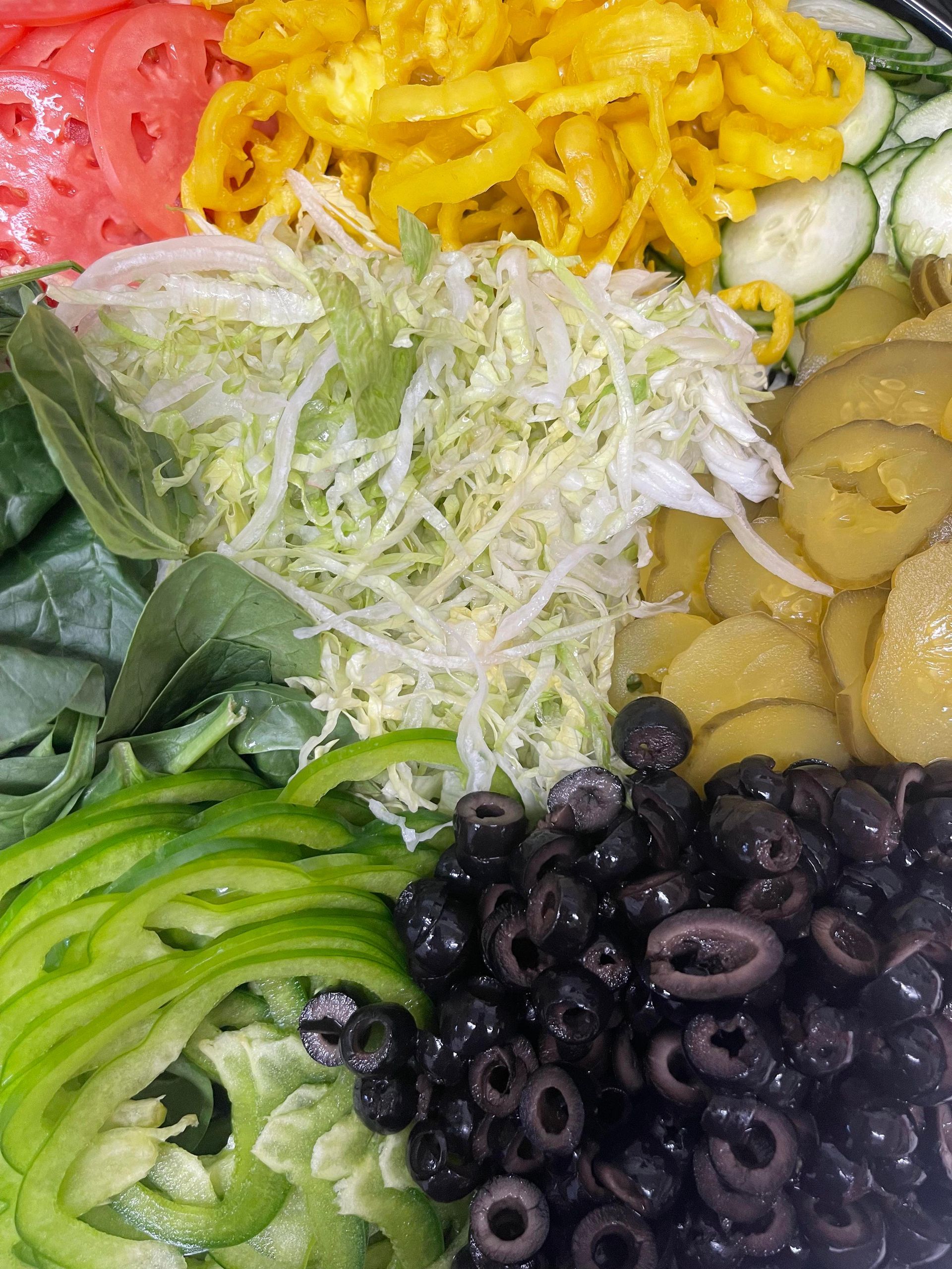 A close-up of a vibrant salad featuring shredded lettuce, sliced black olives, green peppers, tomatoes, and pickles.