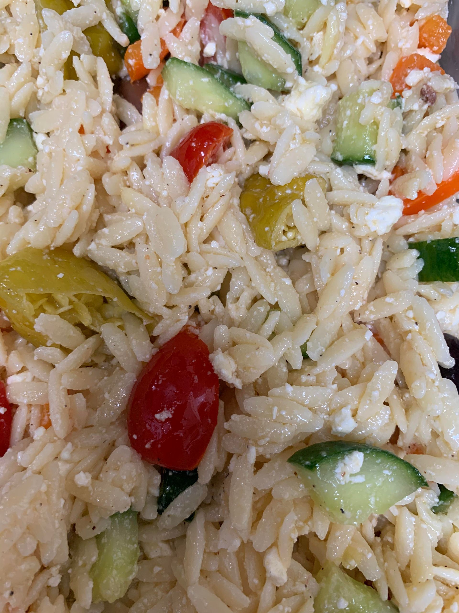 Close-up view of orzo pasta salad with diced cucumbers, cherry tomatoes, and crumbled feta cheese.