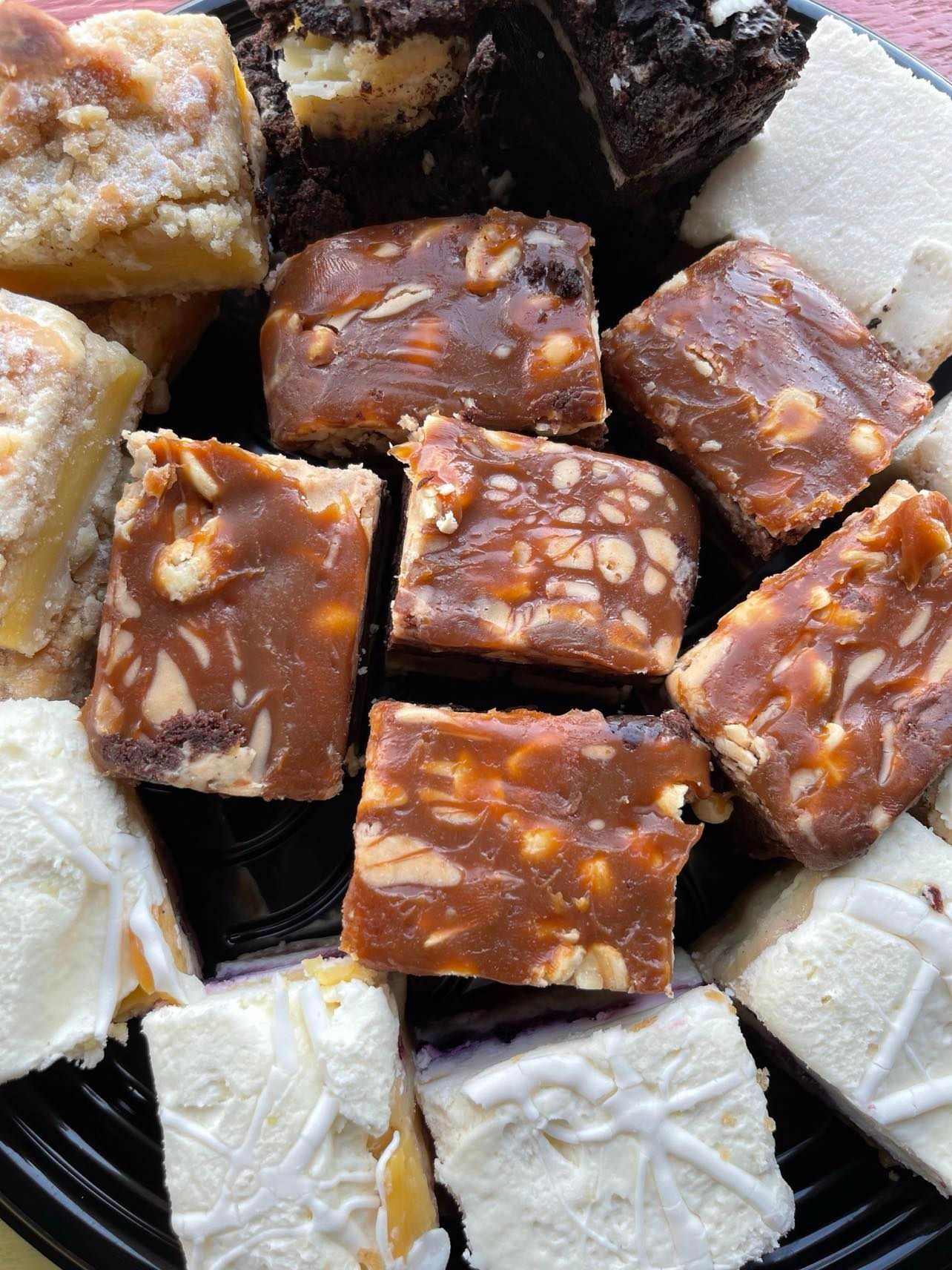 A tray of assorted dessert bars including caramel nut squares, dark chocolate brownies, and white frosted treats.