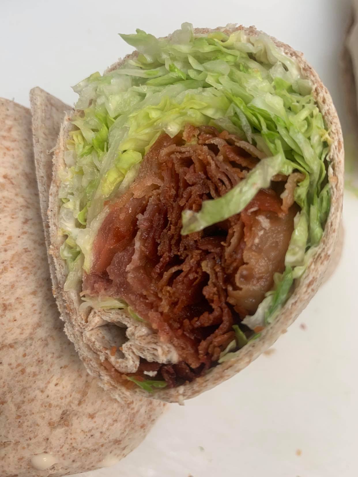 A cross-section of a wrap featuring shredded lettuce and several folded slices of cooked bacon inside a whole-wheat tortilla.