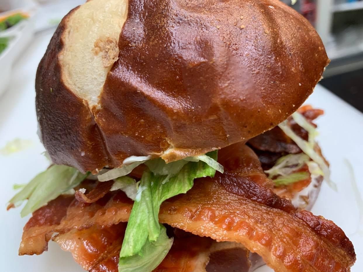 A bacon sandwich on a pretzel bun with shredded lettuce, served on a white plate.