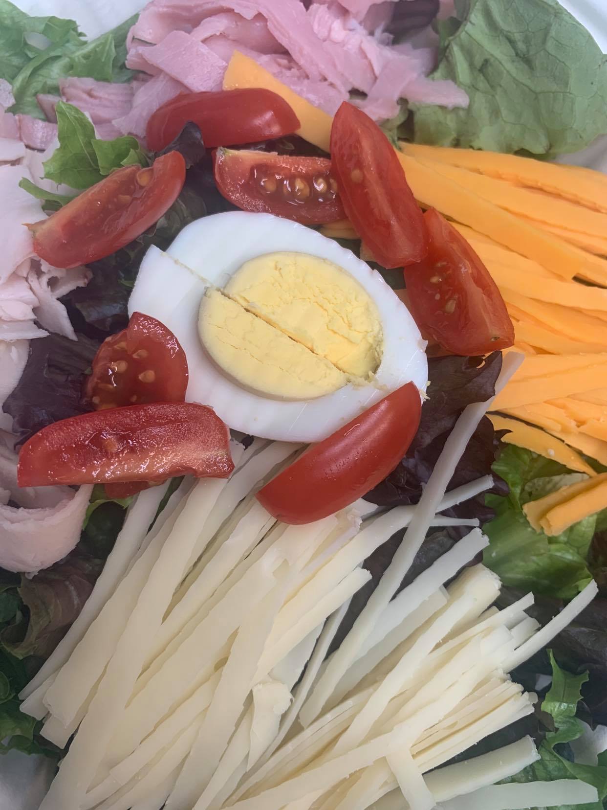 A chef-style salad featuring mixed greens, ham, hard-boiled egg, cherry tomatoes, and strips of cheddar and Swiss cheese.